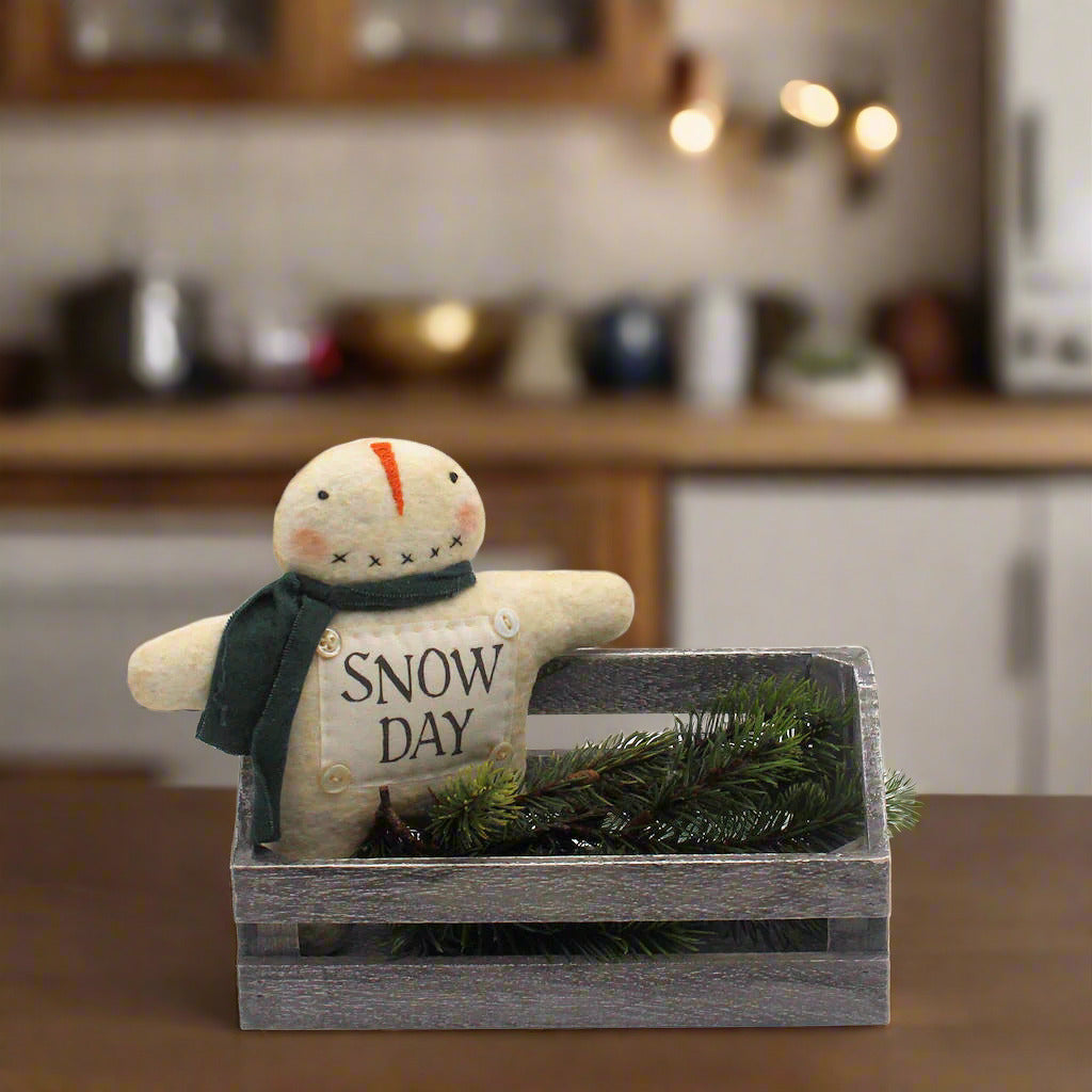 Decorative snowman figurine with 'Snow Day' text in a wooden box on a kitchen counter.
