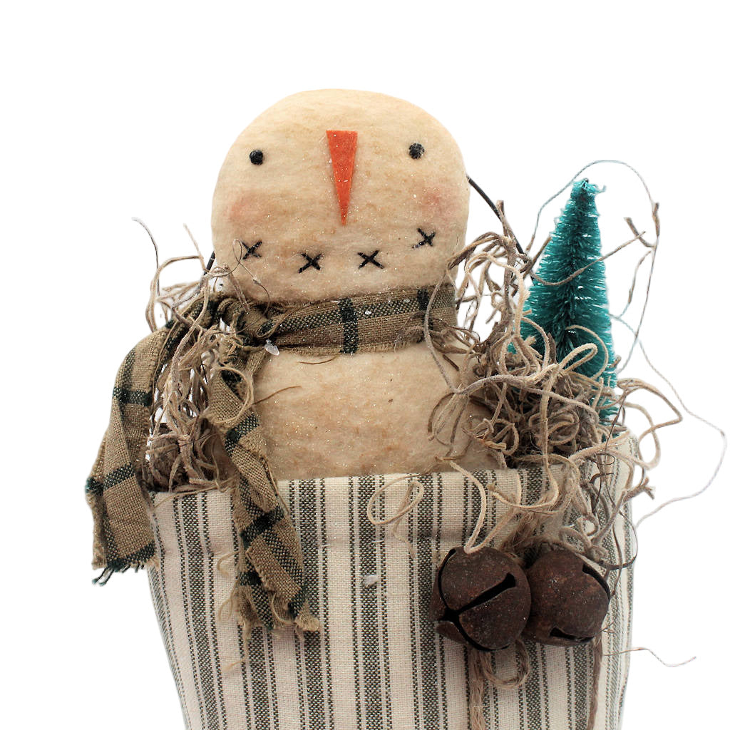 Textile scarecrow figure with plaid scarf, striped stocking, and small tree on a white background
