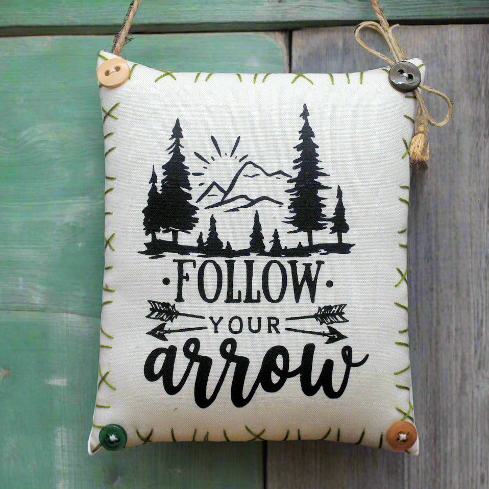 Decorative sign with 'Follow Your Arrow' text and forest design, hanging against a natural background.