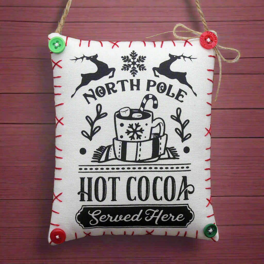 Fabric mini pillow sign with 'North Pole Hot Cocoa Served Here' text and Christmas-themed graphics