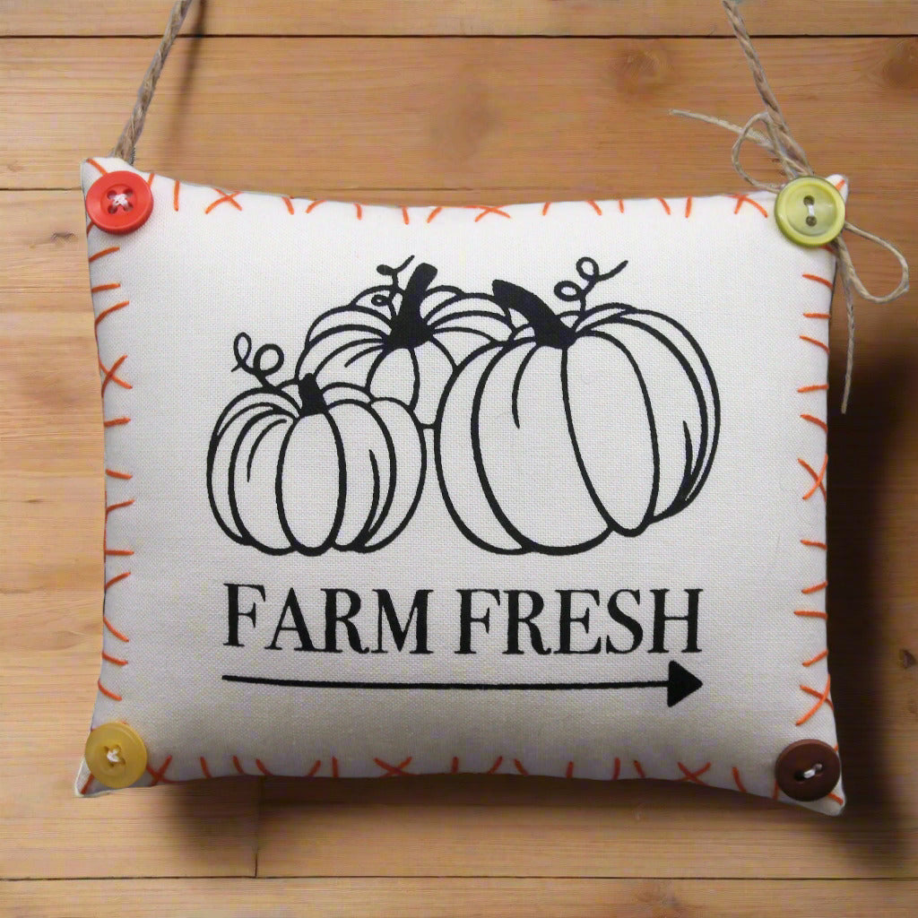Decorative pillow sign with pumpkins and 'Farm Fresh' text on a wooden background