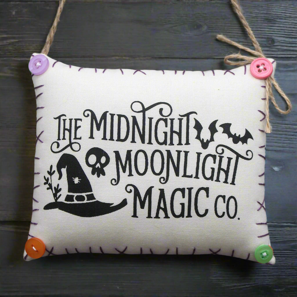 Decorative pillow sign with 'The Midnight Moonlight Magic Co.' text