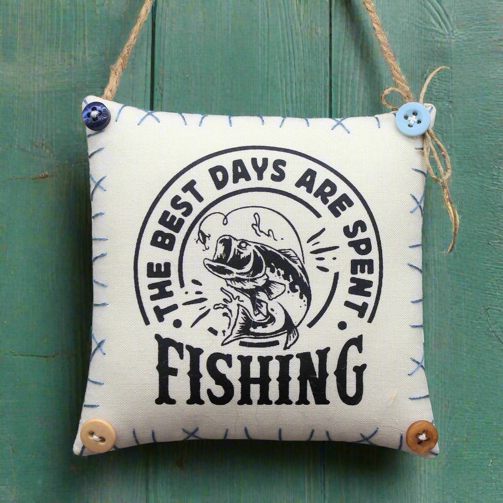 Small pillow with 'The best days are spent fishing' text and fish illustration on a green wooden background