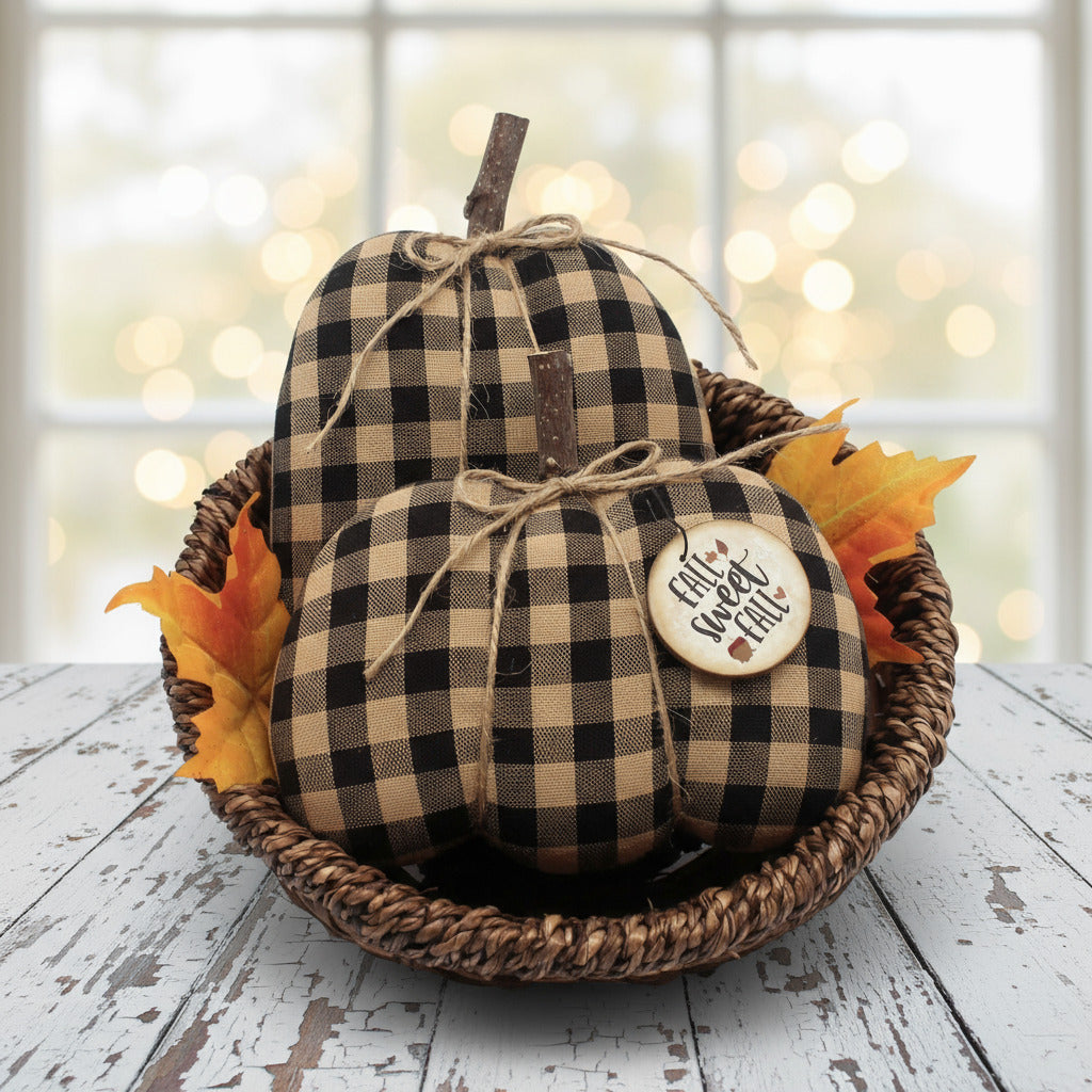 Decorative fabruc pumpkins with checkered pattern and 'Autumn Harvest' tag in a woven basket on a wooden surface.