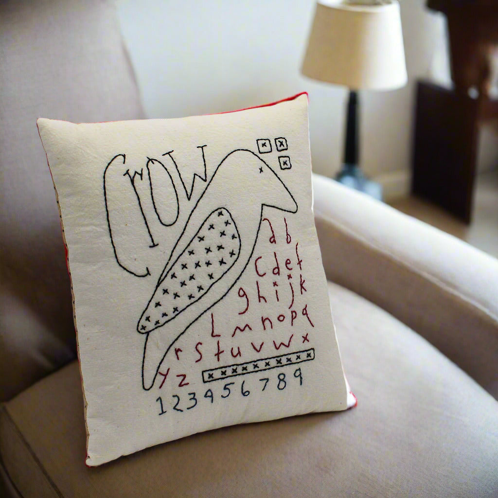 Decorative pillow with a crow illustration and alphabet on a white background