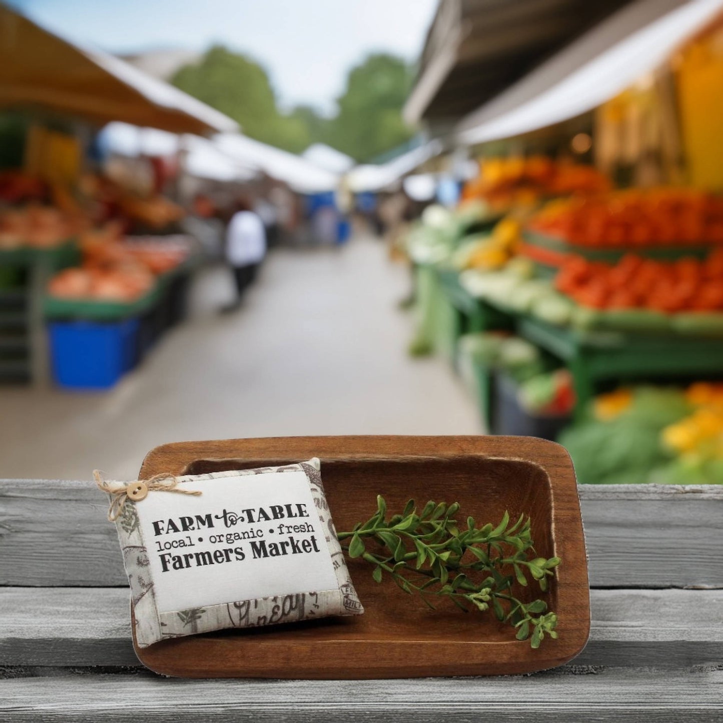 Wooden tray with a 'Farm to Table' sign and fresh herbs at an outdoor farmers market.