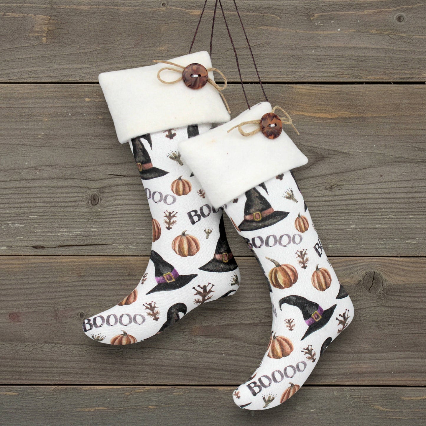 Halloween-themed stocking ornaments with pumpkins, witch hats, and 'BOO' text on a wooden background.