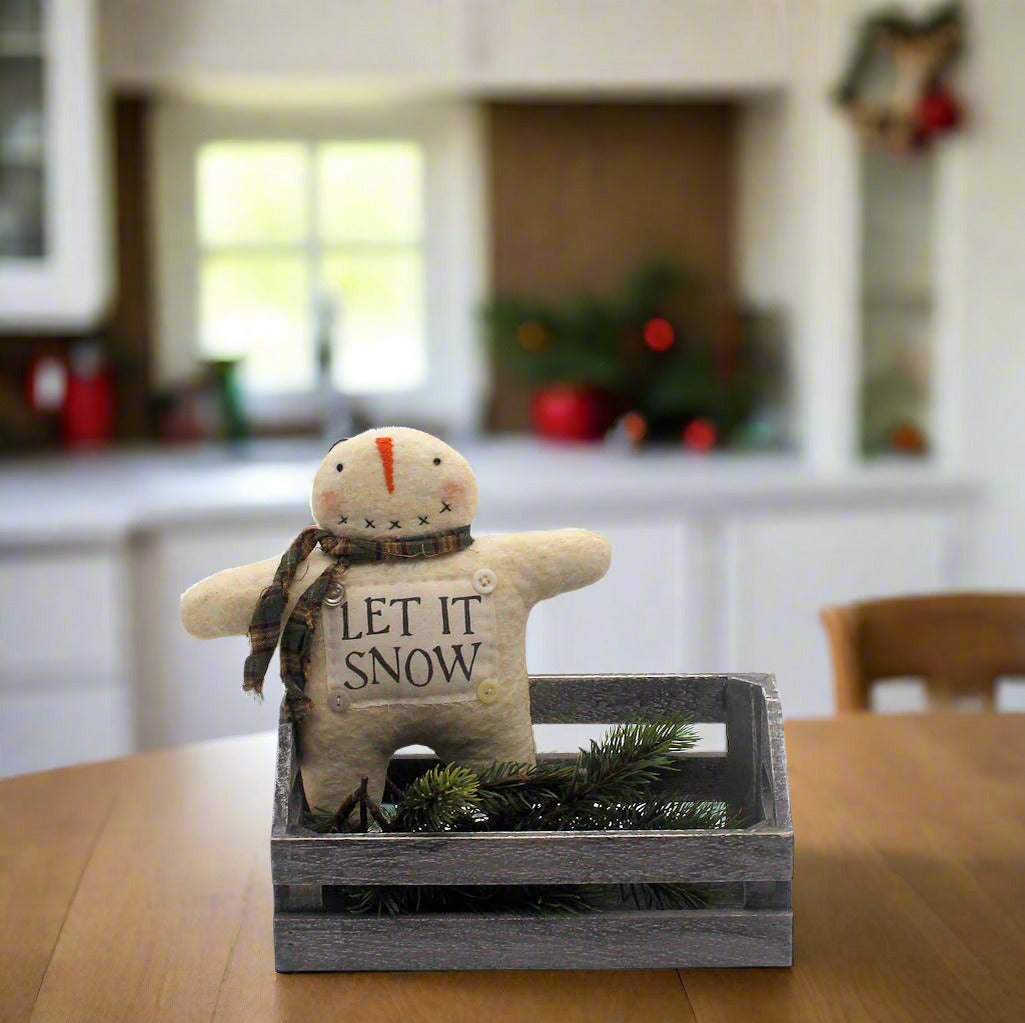 Small snowman figurine with 'Let It Snow' text in a wooden crate