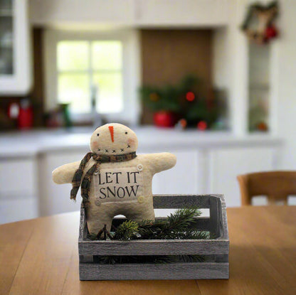 Small snowman figurine with 'Let It Snow' text in a wooden crate