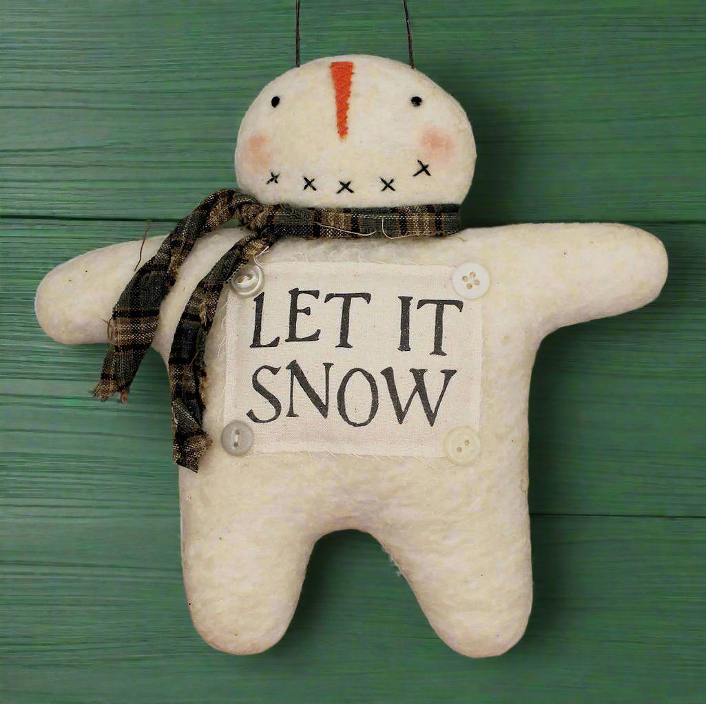 Textile snowman ornament with 'LET IT SNOW' sign on a green wooden background
