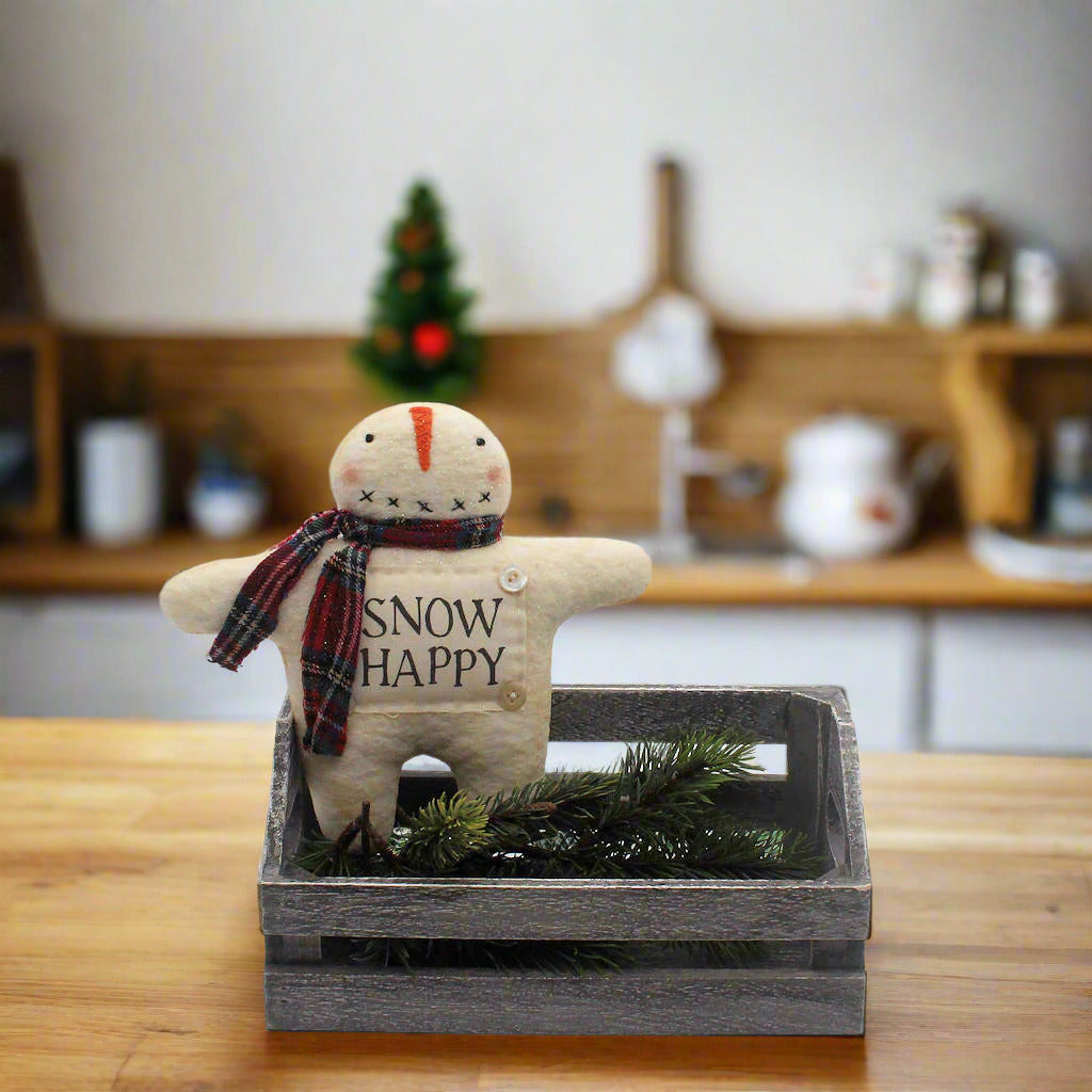 Small snowman figurine with a plaid scarf and 'Snow Happy' text in a wooden crate