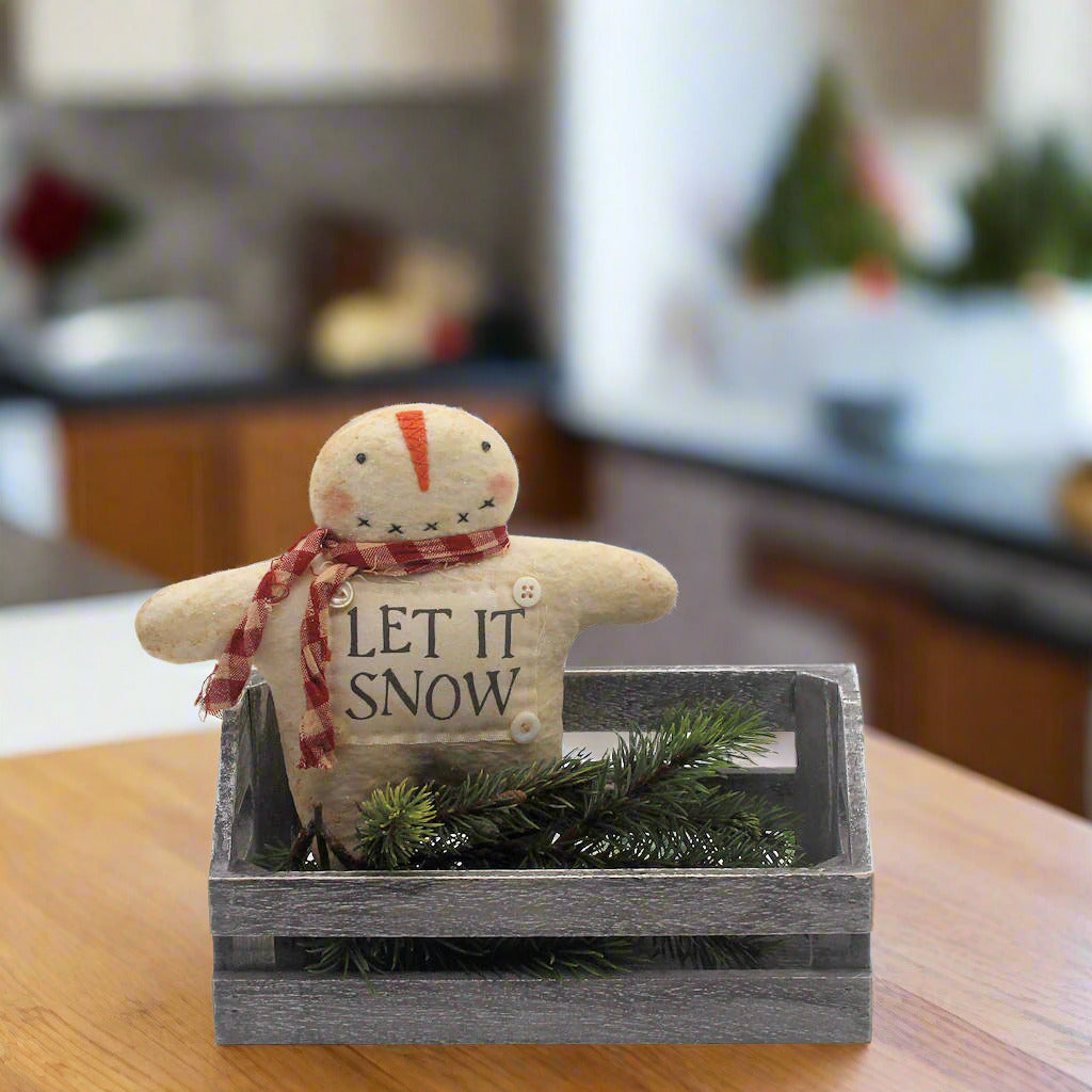 Primitive snowman ornament with a scarf and 'LET IT SNOW' text in a wooden crate