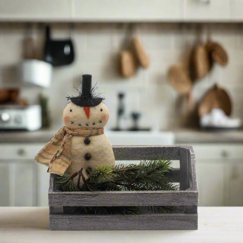 Decorative primitive snowman with a black top hat and brown scarf in a wooden crate