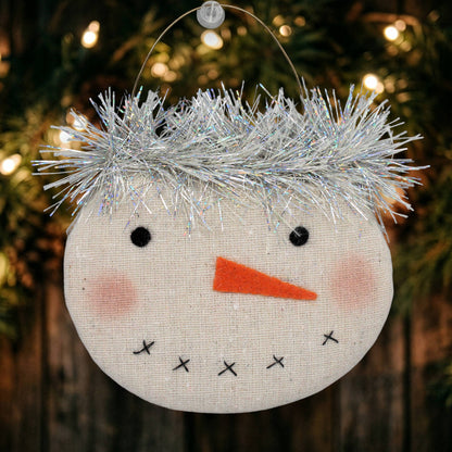 Decorative snowman ornament with tinsel hair on a Christmas tree.