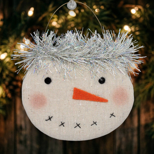 Decorative snowman ornament with tinsel hair on a Christmas tree.