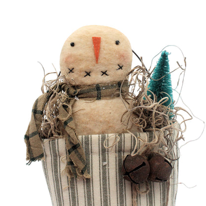 Textile scarecrow figure with plaid scarf, striped stocking, and small tree on a white background