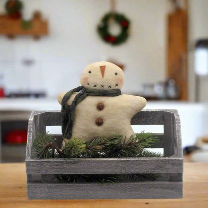 Primitive snowman ornament with a green scarf in a wooden crate