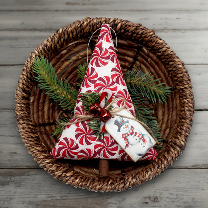 Decorative Christmas tree ornament with red and white pattern on a woven plate with greenery.