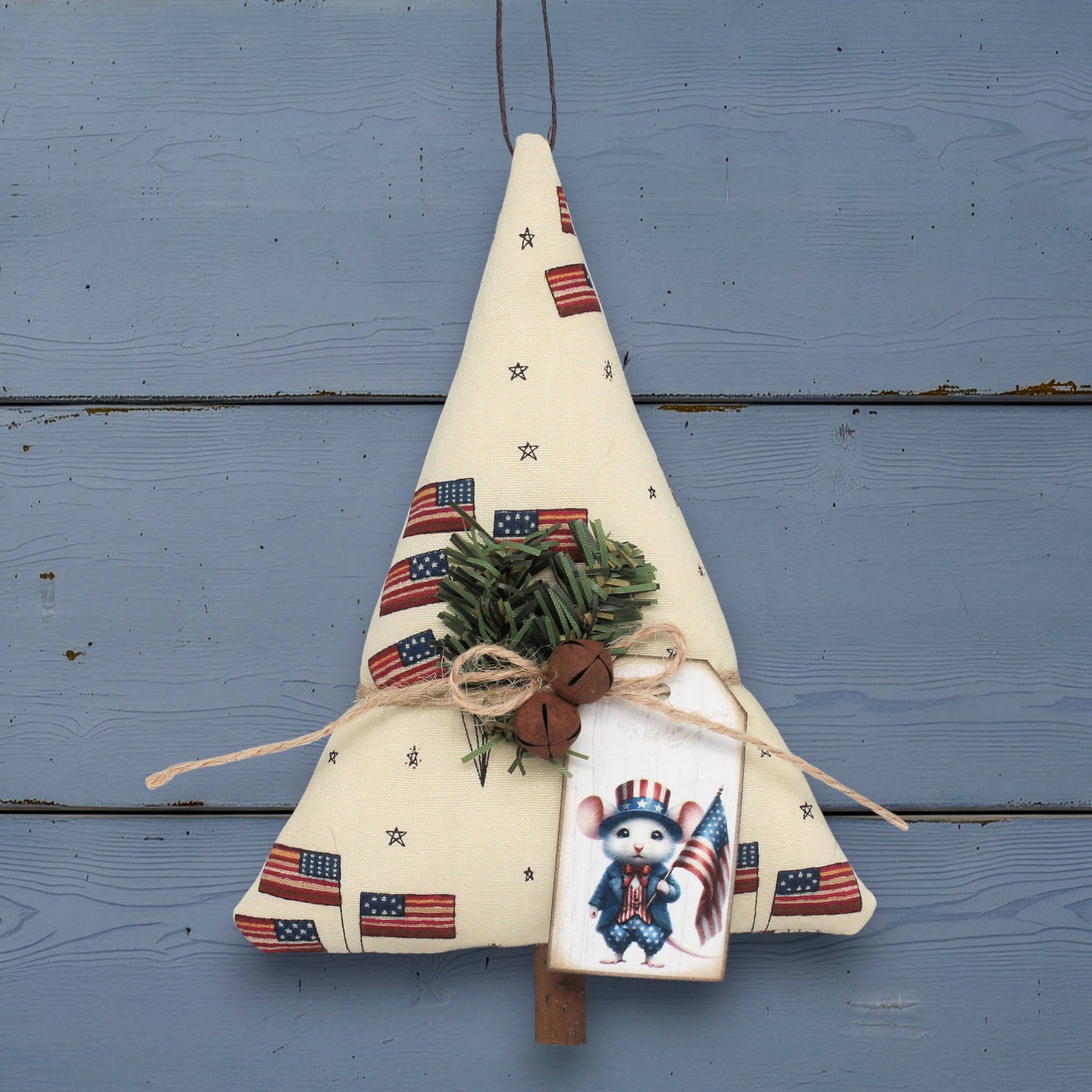 Decorative Christmas tree-shaped ornament with American flag patterns and a small figurine on a blue wooden background.