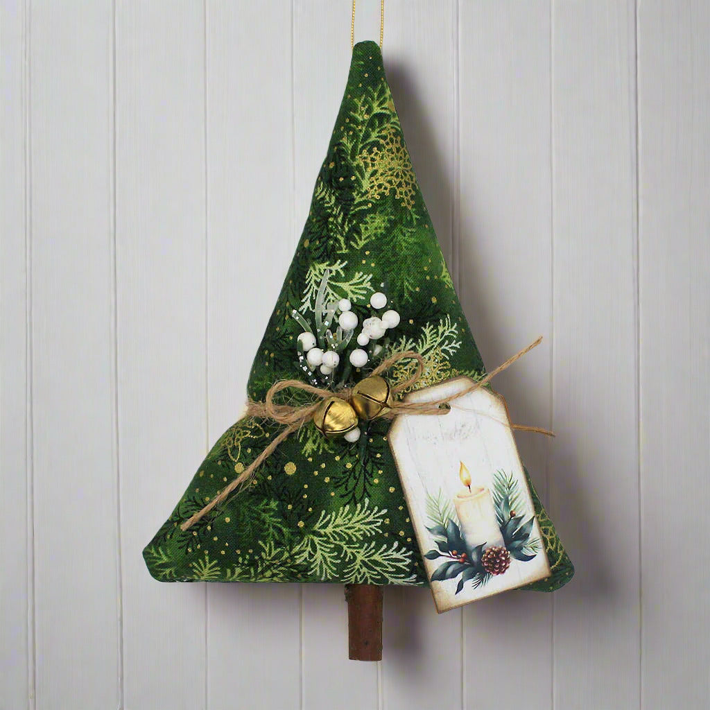 Decorative Christmas tree ornament with green fabric, gold jingle bells, and a small tag on a white background.