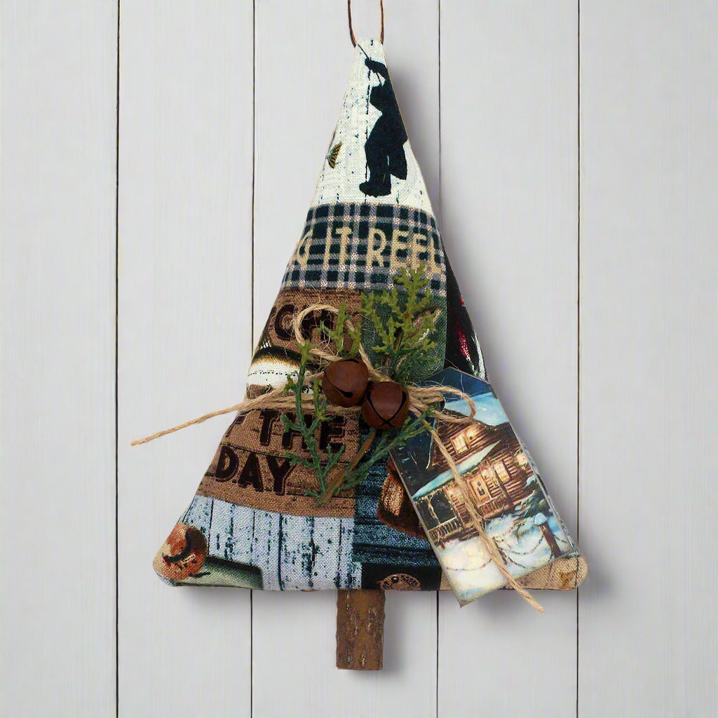 Tree-shaped ornament sewn from cotton print fabric with a fishing cabin design, with rusty bells, greenery and a tag