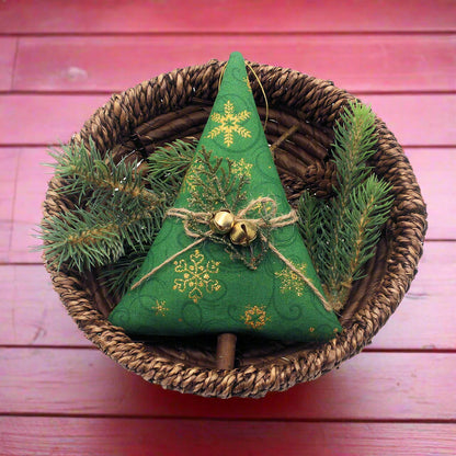 Green fabric Christmas tree with gold snowflakes and jingle bells in a woven basket with greenery.