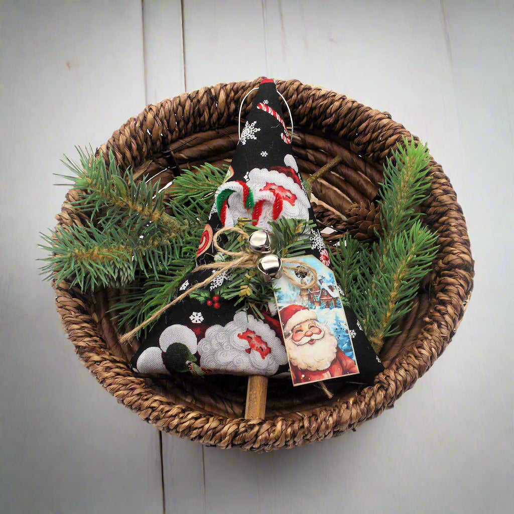 Decorative Christmas ornament with a Santa tag in a woven basket with greenery on a white background