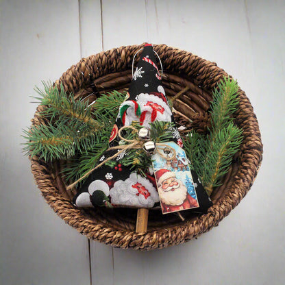Decorative Christmas ornament with a Santa tag in a woven basket with greenery on a white background
