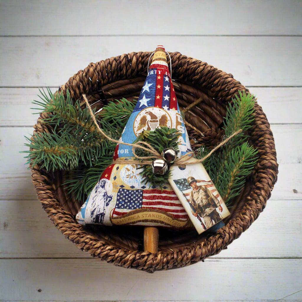 Decorative Christmas tree ornament with American flag design in a woven basket with greenery.
