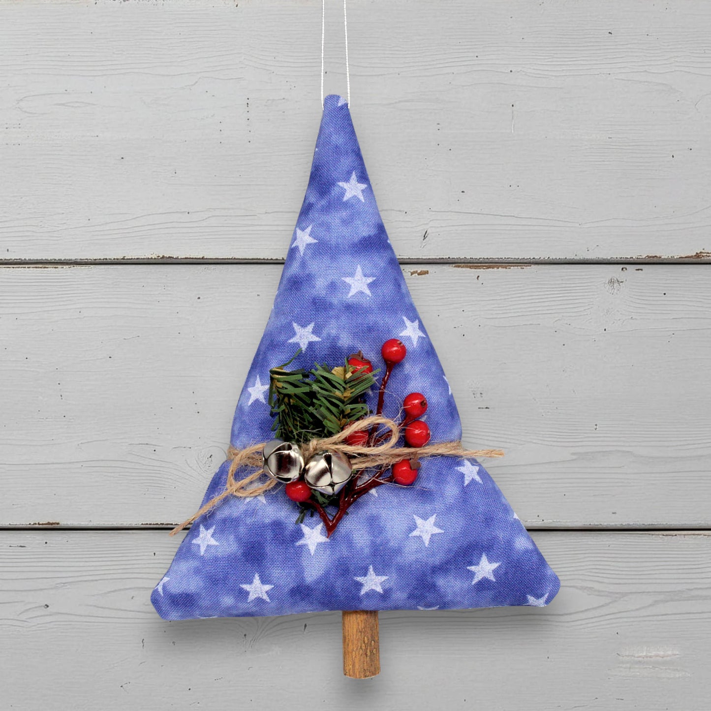 Blue fabric Christmas tree decoration with white stars, red berries, and greenery on a wooden background.