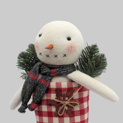 Decorative primitive snowman in a red and white homespun stocking along with pine and a rusty snowflake