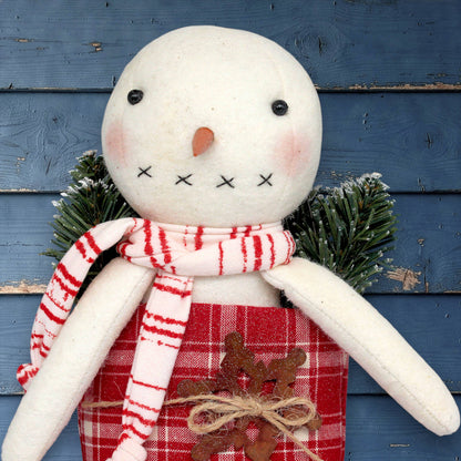 Handmade snowman with a red scarf and plaid pants against a blue wooden background