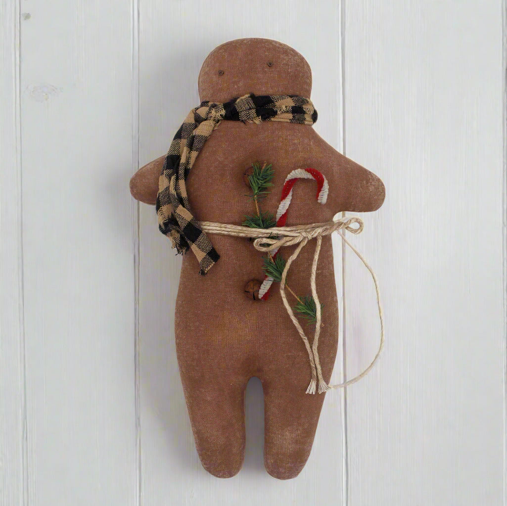 Primitive gingerbread man cookie doll with a plaid scarf, candy cane, and greenery on a white background