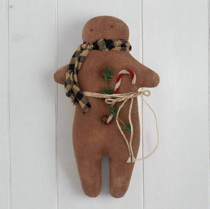 Primitive gingerbread man cookie doll with a plaid scarf, candy cane, and greenery on a white background