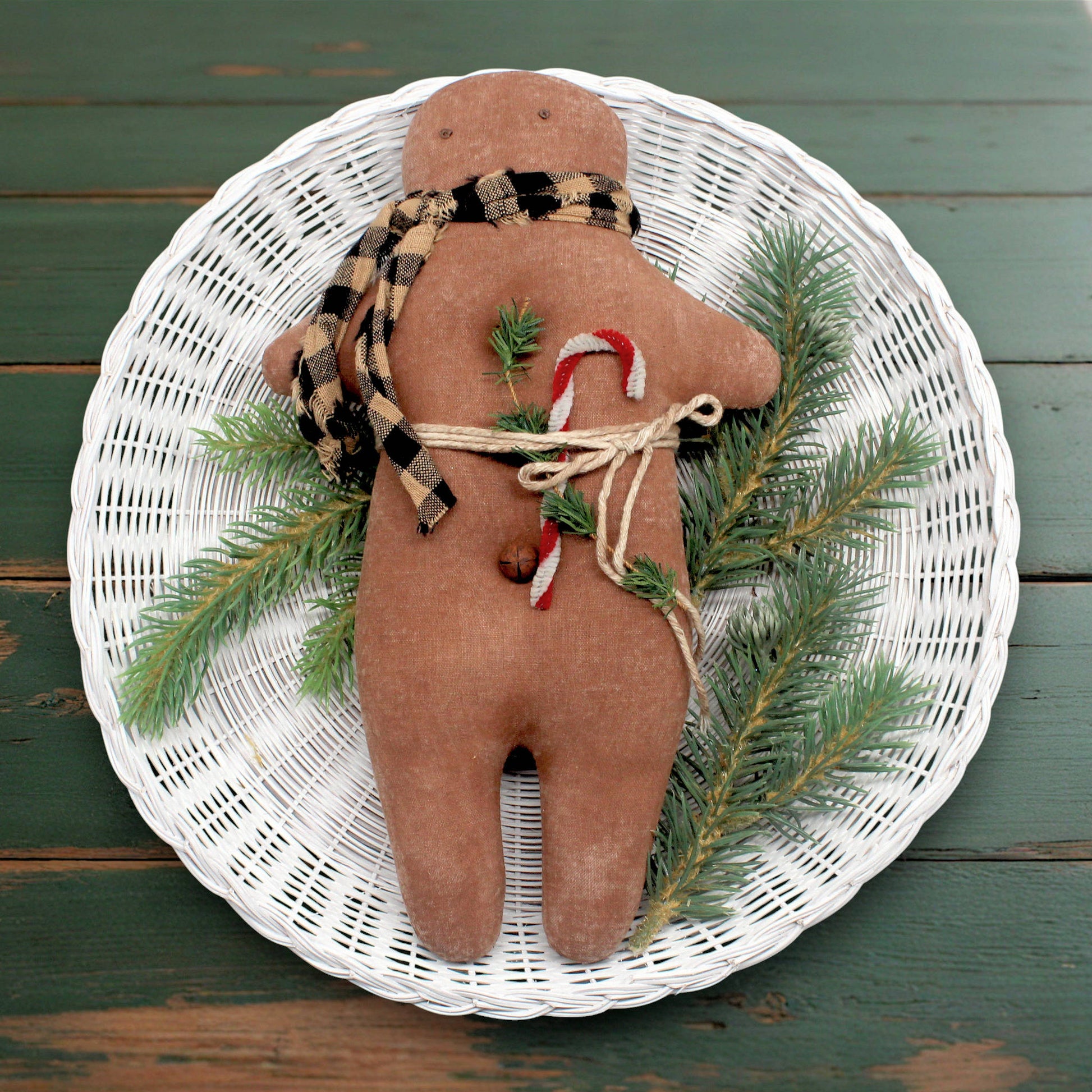 Primitive gingerbread doll with Christmas elements on a white woven plate against a wooden background