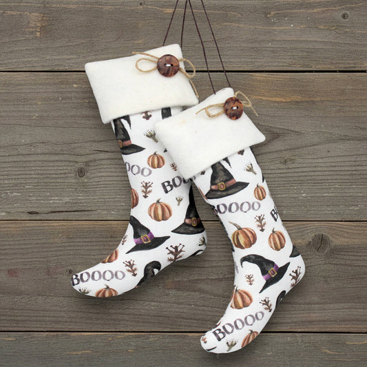 Halloween-themed stocking ornaments with pumpkins, witch hats, and 'BOO' text on a wooden background.