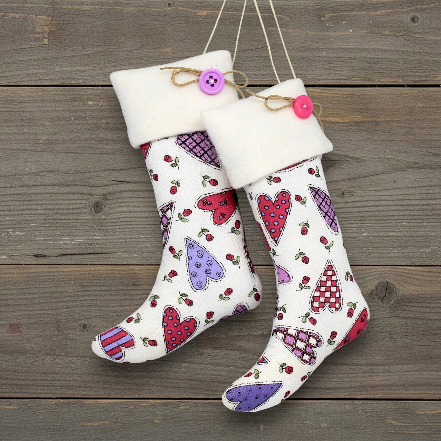 Pair of Christmas stocking ornaments with pink and purple hearts on a white background