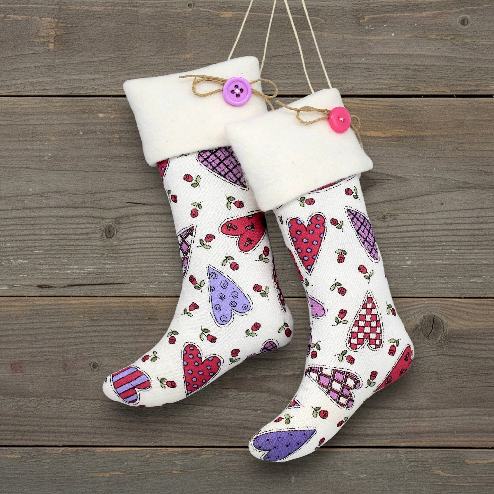 Pair of Christmas stocking ornaments with pink and purple hearts on a white background