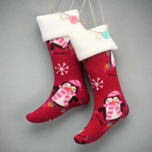 Christmas stocking ornaments with cute penguins on a dark pink background with white cuffs decorated with buttons