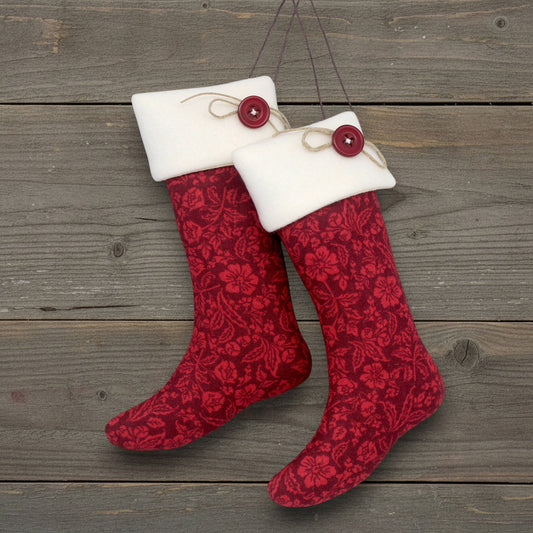 Red patterned Christmas stocking ornaments with white cuffs and red buttons on a wooden surface