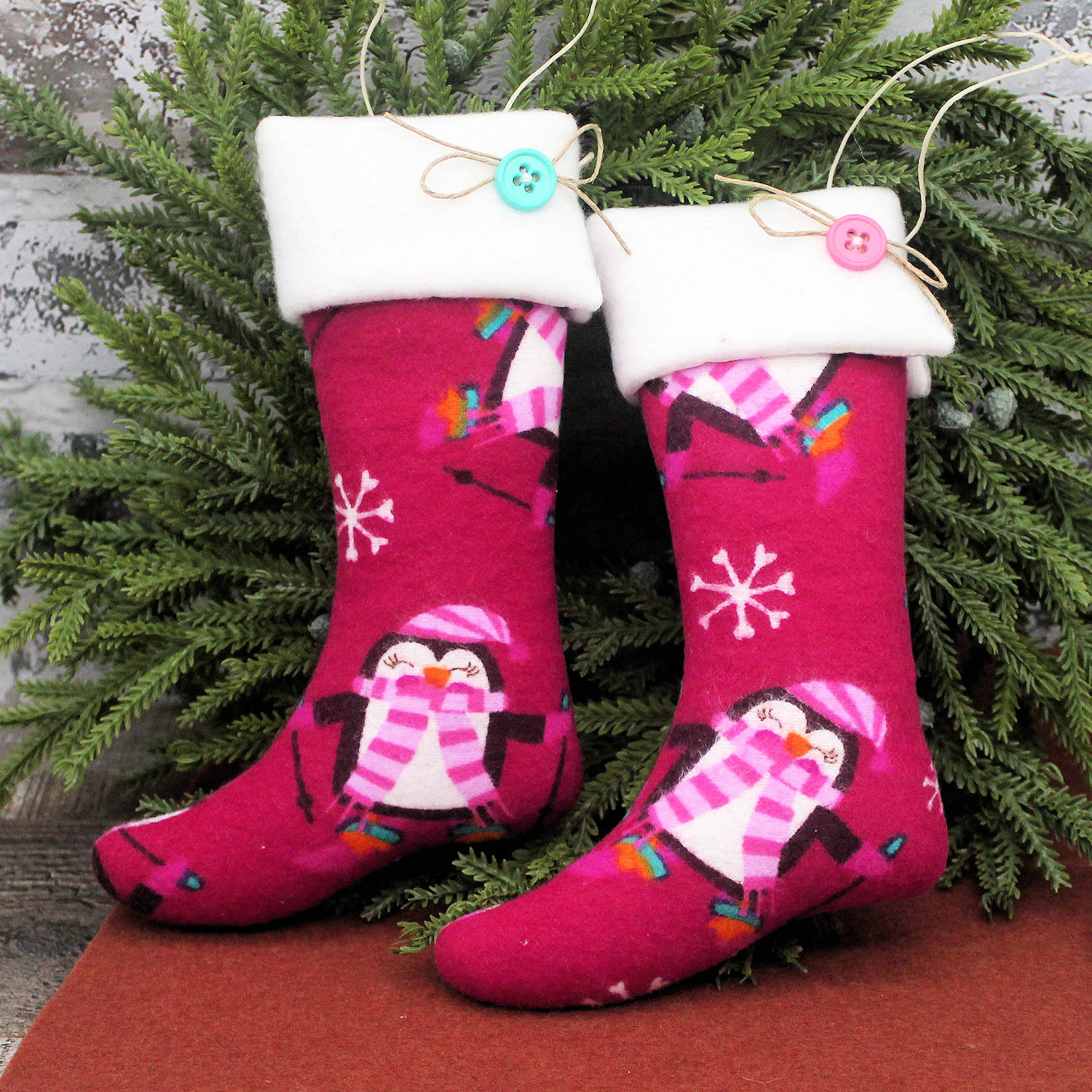 Two pink Christmas stockings with penguin designs against a green leafy background.
