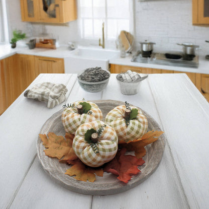 Decorative fabric pumpkins on a wooden plate with fall leaves in a kitchen setting.