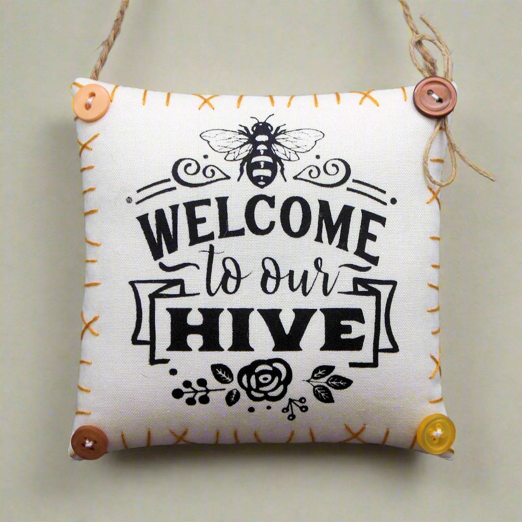 Decorative pillow with 'Welcome to our Hive' text and bee design on a plain background