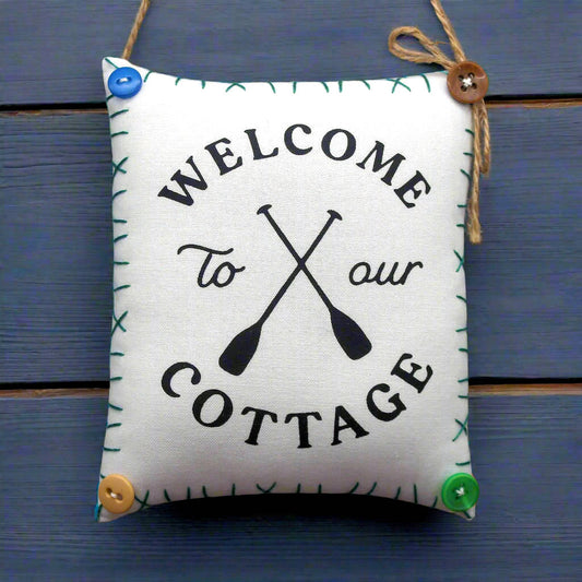 Decorative sign with 'Welcome to our Cottage' text and oar design on a blue wooden background.