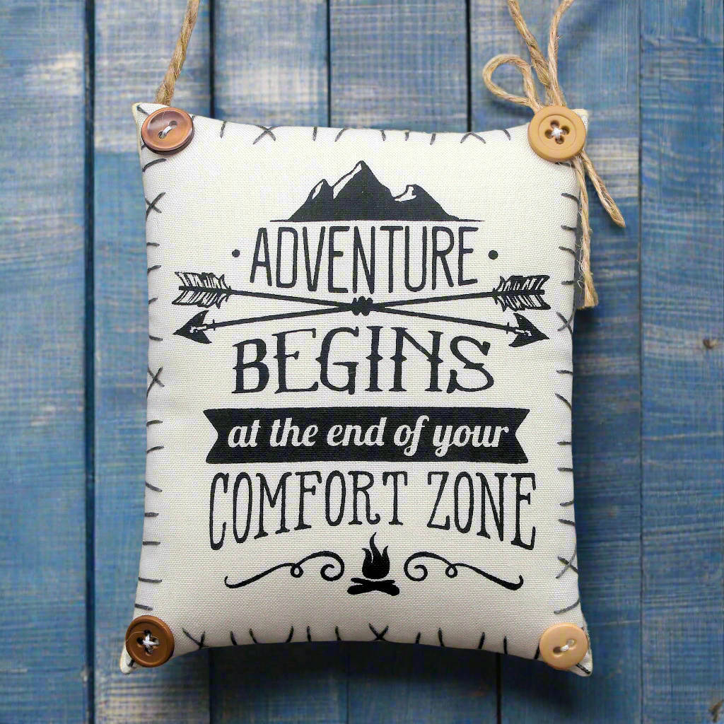 Decorative sign with 'Adventure Begins at the End of Your Comfort Zone' text on a blue wooden background