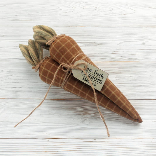 Three homespun fabric carrots tied in a bundle with a tag on a white wooden background
