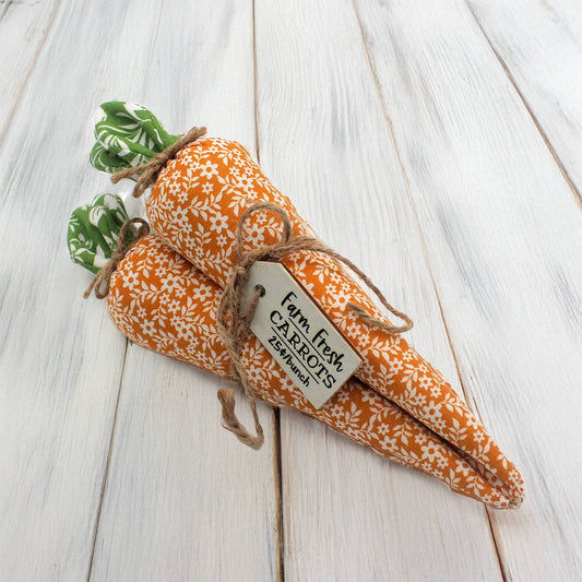 Three fabric carrots tied in a bundle with a tag on a wooden surface