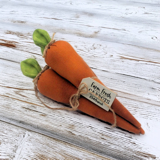 Three plush carrots tied in a bundle with a tag on a wooden surface