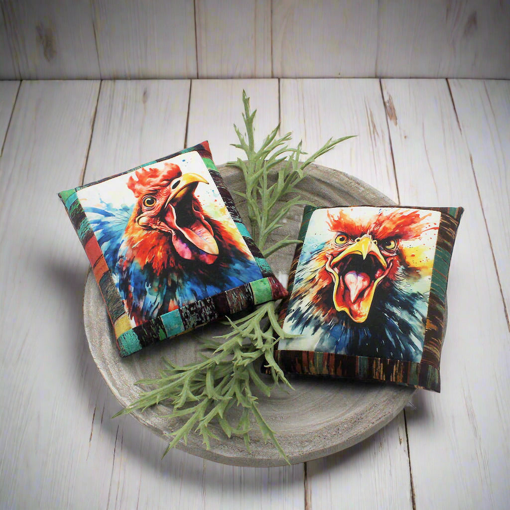Two colorful rooster pillows on a wooden plate with greenery.