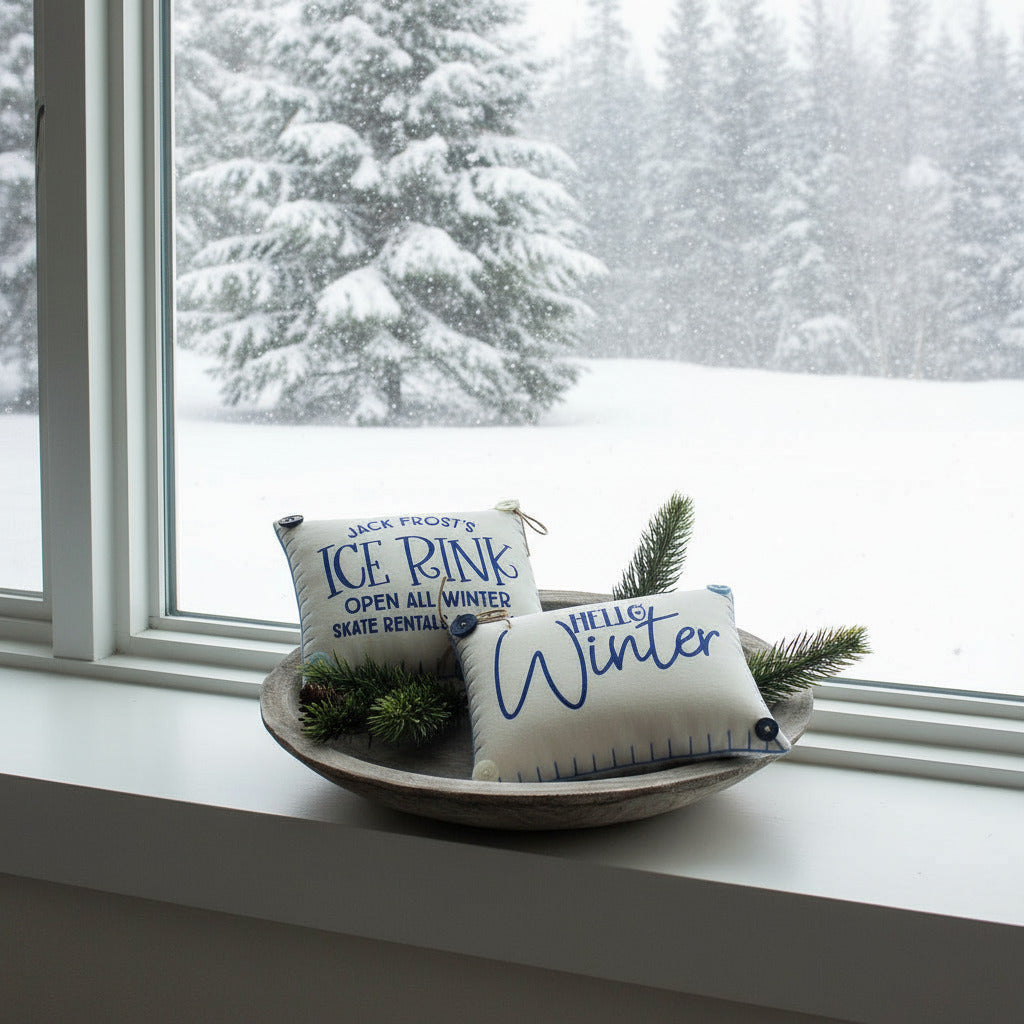 Two decorative mini pillows with text on a wooden plate with pine branches